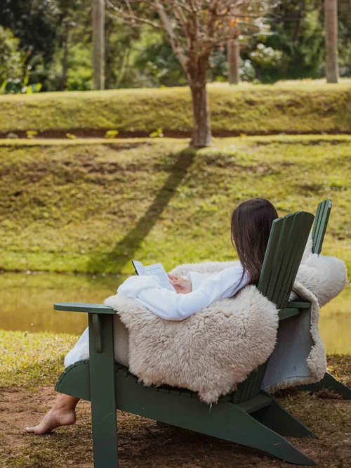 Mulher lendo em cadeira junto ao lago